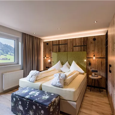 Ein modernes Schlafzimmer mit einem großen Bett und rustikalem Holzdekor. Große Fenster bieten Blick auf die Landschaft.