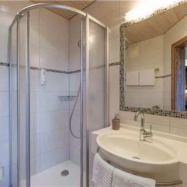 Ein modernes Badezimmer mit einer Dusche und einem Waschbecken. Die Wände sind mit hellen Fliesen gestaltet und es gibt einen großen Spiegel.