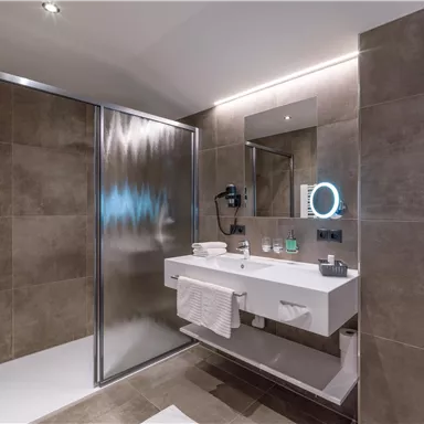 Ein modernes Badezimmer mit einer Dusche und einem stilvollen Waschbecken. Die Wände sind in einem eleganten Braunton gehalten, und es gibt ausreichend Licht.