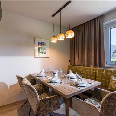 Ein gemütlicher Essbereich mit einem Holztisch und eleganten Stühlen. Weiche Beleuchtung und eine schöne Aussicht durch das Fenster schaffen eine einladende Atmosphäre.