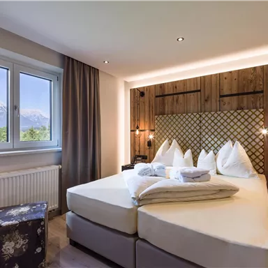 Ein modernes Schlafzimmer mit einem gemütlichen Doppelbett und großen Fenstern, die eine schöne Aussicht auf die Berge bieten. Die warmen Holzelemente schaffen eine einladende Atmosphäre.
