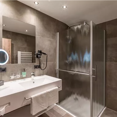 Ein modernes Badezimmer mit einer Glastür-Dusche und einem stilvollen Waschbecken. Der Raum ist in neutralen Farben gehalten und verfügt über eine schöne Beleuchtung.