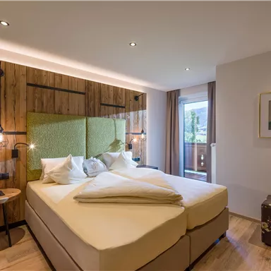 Ein modernes Schlafzimmer mit einem großen Bett und Holzdekor. Große Fenster ermöglichen viel Tageslicht und bieten einen Blick nach draußen.