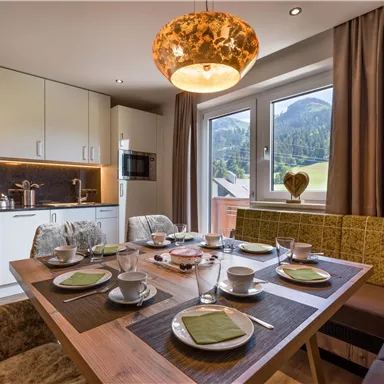 Eine moderne Küche mit einem Esstisch, der für das Frühstück gedeckt ist. Große Fenster bieten einen Blick auf die bergige Landschaft.