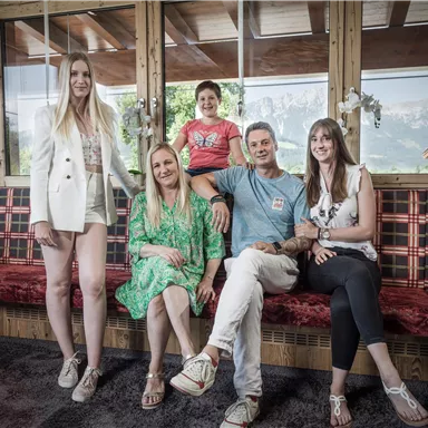 Eine Gruppe von fünf Personen sitzt in einem gemütlichen Raum. Der Raum hat eine rustikale Einrichtung mit Holz und einem Blick auf die Natur.