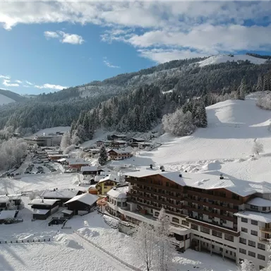 Eine winterliche Landschaft mit schneebedeckten Hügeln und einem kleinen Dorf. Die Gebäude sind in eine ruhige, weiße Decke aus Schnee eingebettet.