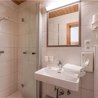 A modern bathroom with a shower, a hand wash basin, and a large mirror. The walls are brightly tiled and there are fresh towels.