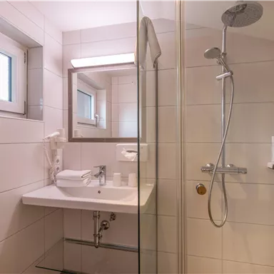 A modern bathroom with a shower and a sink. The walls are brightly tiled, and there is plenty of natural light coming through the window.