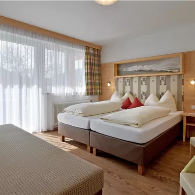 A cozy hotel room with two single beds and a comfortable sofa. Large windows provide plenty of daylight and a warm atmosphere.