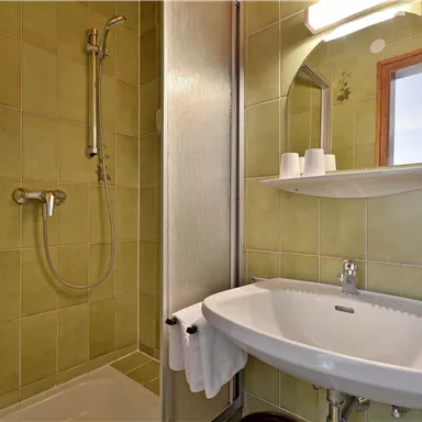 A small bathroom with a shower and a sink. The walls are in a light green tone.