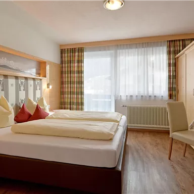 A cozy hotel room with a double bed and two armchairs. Large windows provide plenty of daylight and a bright atmosphere.