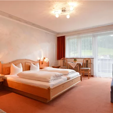 A cozy bedroom with a double bed and a small living area. Large windows provide plenty of natural light.