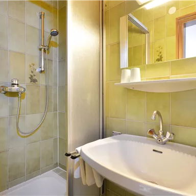 A modern bathroom with a shower and a sink. The walls are a light green color.