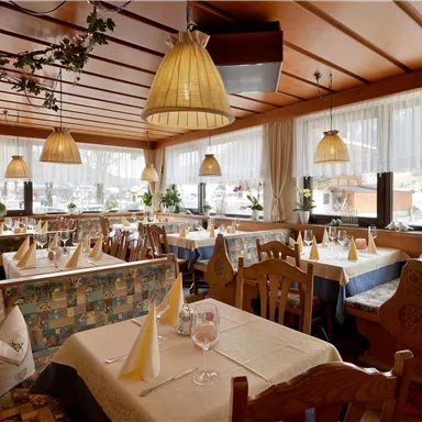 A cozy restaurant with wooden furniture and sunny light. The tables are beautifully set, and there are plants at the windows.