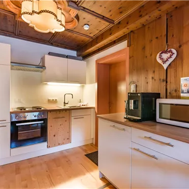 Eine moderne Küche mit Holzverkleidung und hellem Licht. Die Ausstattung umfasst einen Herd, eine Mikrowelle und viel Stauraum.