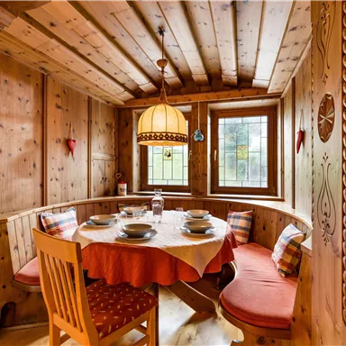 Ein gemütlicher Essbereich mit Holzwänden und einem runden Tisch. Die Sitzbänke sind mit bunten Kissen dekoriert und eine Lampe hängt von der Decke.