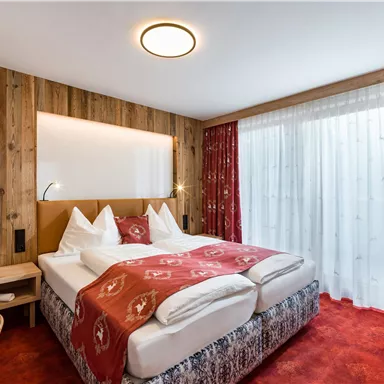 Ein gemütliches Schlafzimmer mit einem Doppelbett und holzverkleideten Wänden. Große Fenster sorgen für viel Tageslicht und es gibt eine freundliche, behagliche Atmosphäre.