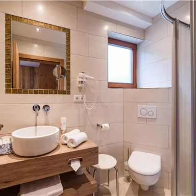 Ein modernes Badezimmer mit einer Dusche, einem Waschbecken und WC. Die Wände sind hell gefliest, und es gibt große Fenster für natürliches Licht.