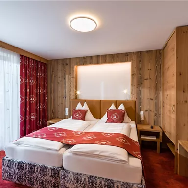 Ein gemütliches Schlafzimmer mit zwei Betten und Holzverkleidung. Die Einrichtung ist modern und einladend mit rotem Teppich und Vorhängen.