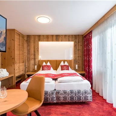 Ein gemütliches Hotelzimmer mit zwei Betten und Holzvertäfelung. Das Zimmer ist hell und freundlich mit großen Fenstern und einem kleinen Tisch.