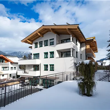 A modern building in alpine style, surrounded by snow. The sky is partly cloudy, with a view of the mountains.