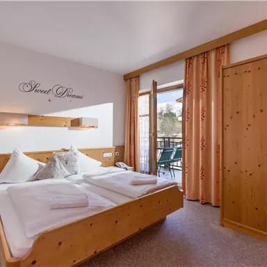 Ein gemütliches Schlafzimmer mit zwei Betten, Holzverkleidung und einem Balkon. Große Fenster lassen viel Licht hereingehen und bieten einen Blick nach draußen.