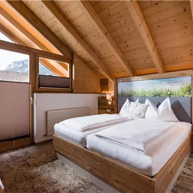 Ein gemütliches Schlafzimmer mit Holzwänden und einem Dachfenster. Es ist mit einem Doppelbett und einem schönen Landschaftsbild dekoriert.