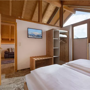 Ein gemütliches Schlafzimmer mit zwei Einzelbetten und Holzmöbeln. Das Zimmer hat große Fenster mit Blick auf die Berge und einen bequemen Sitzbereich.