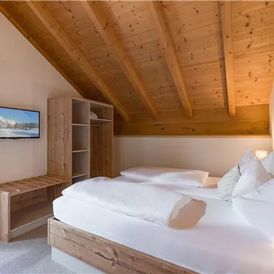Ein gemütliches Schlafzimmer mit zwei Betten und Holzdecke. Der Raum ist hell, mit einem Fernseher und einem kleinen Schreibtisch aus Holz.