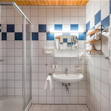 Ein modernes Badezimmer mit Duschecke und weißem Waschbecken. Die Wände sind mit weißen Fliesen und blauen Akzenten dekoriert.