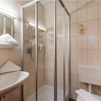 Ein modernes Badezimmer mit Dusche und Waschbecken. Die Wände sind hell gefliest, und es gibt frische Handtücher.