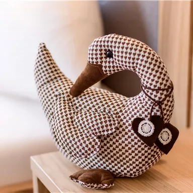 Eine kuschelige Entenfigur aus Stoff sitzt auf einem Tisch. Sie hat ein braun-weißes Muster und einen süßen Ausdruck.