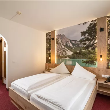 A cozy bedroom with a large bed and a beautiful mural of mountains by a lake. The room has a warm atmosphere with soft lighting.
