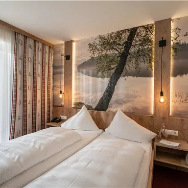 A modern hotel room with two single beds and a stylish wall motif of a lake. Soft lighting and large windows create a bright, inviting atmosphere.