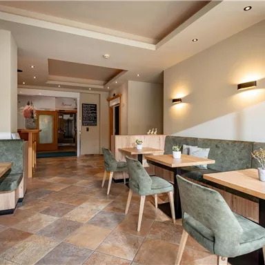 A modern restaurant interior with wooden and green seating. The walls are painted in neutral colors and there are well-lit boards.