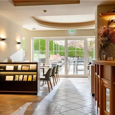 An inviting reception area with bright walls and a modern counter. Large windows provide a view of a terrace with outdoor seating.
