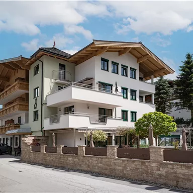 Ein modernes Gebäude im alpinen Stil mit Holzelementen. Es befindet sich an einer Straße, umgeben von Bäumen und einer schönen Landschaft.