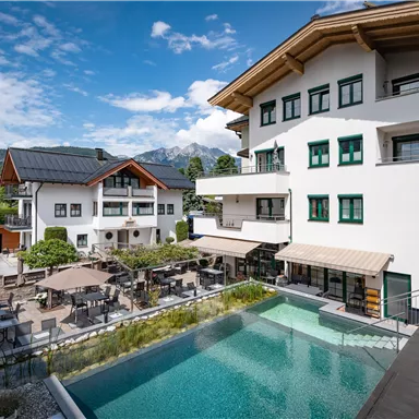 Ein modernes Hotel mit einem schönen Außenbereich und einem Pool. Im Hintergrund sind grüne Wiesen und Berge zu sehen.