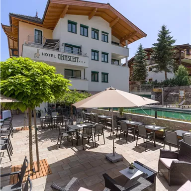 Ein elegantes Hotel mit einem schönen Außenbereich und komfortablen Möbeln. Die Terrasse ist mit SonnenSchirmen und Pflanzen dekoriert.
