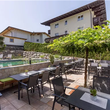 Ein hübscher Außenbereich mit Tischen und Stühlen neben einem Pool. Im Hintergrund stehen einige Gebäude und Bäume.