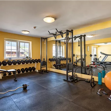 A modern gym with weights and training equipment. The walls are painted yellow and there are large mirrors as well as some fitness balls.