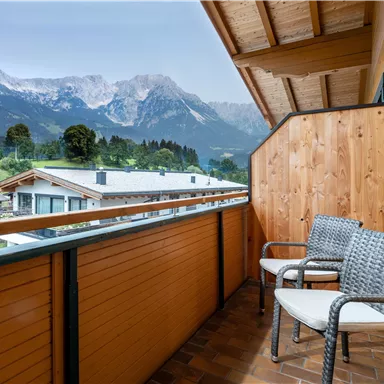 A cozy balcony with two chairs and a view of the mountains. The surroundings are quiet and natural.