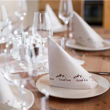 Ein schön gedeckter Tisch mit weißen Servietten und Gläsern. Die Servietten sind elegant gefaltet und mit einem Logo verziert.