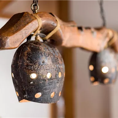 Ein Holzobjekt mit zwei hängenden Lampen aus schwarzem Metall. Die Lampen haben kleine Löcher, durch die das Licht schimmert.
