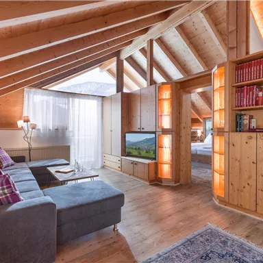 Ein gemütliches Loft mit Holzvertäfelung und großen Fenstern. Der Wohnbereich ist hell und modern eingerichtet, mit einem Fernseher und einem Bücherregal.