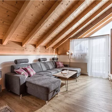 Ein modernes Wohnzimmer mit Holzdecke und bequemen Möbeln. Ein großer Fensterbereich lässt viel Licht herein und bietet einen schönen Ausblick.