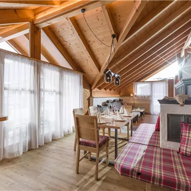 Ein gemütlicher Raum mit Holzdecke und großen Fenstern. Es gibt einen Essbereich mit Tischen und Stühlen sowie eine entspannte Sitzgelegenheit.