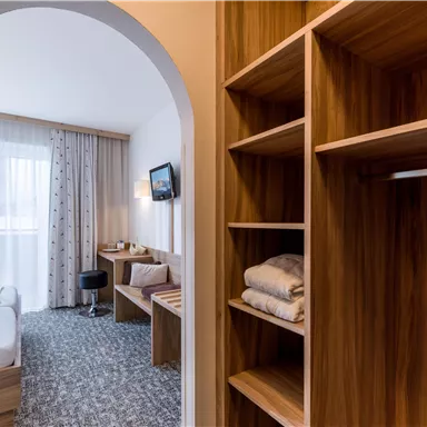 A modern room with a cozy bed and a workspace. The windows let in plenty of light and the wooden shelves provide storage space.