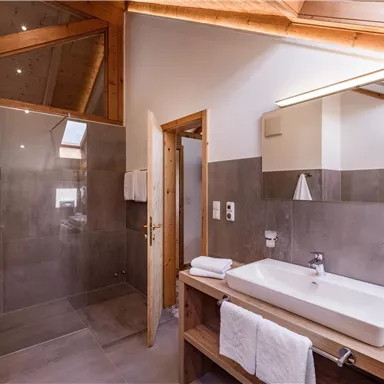 Ein modernes Badezimmer mit einer großen Dusche und einem stilvollen Waschtisch. Helle Wände und Holzdetails sorgen für eine einladende Atmosphäre.