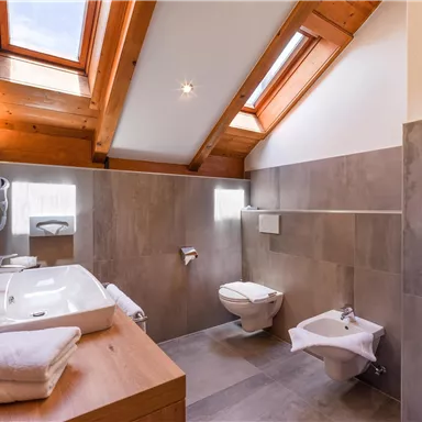 Ein modernes Badezimmer mit Holzdecken und großen Fenstern. Es enthält eine Badewanne, ein WC und elegante Armaturen.